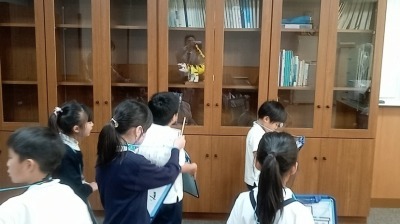 ガラス扉の前に立つ学生帽の小学生たち。背景に本棚が見える。