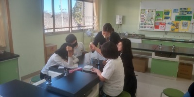 中学校の先生に実験をみてもらいました。屋内で、実験器具を囲むように座る4人の生徒と1人の先生の写真。
