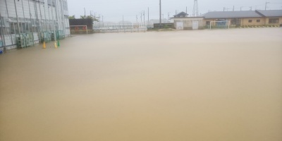 水浸しのグランド。校庭が茶色い水で完全に浸水している様子。背景には校舎や建物が見える。