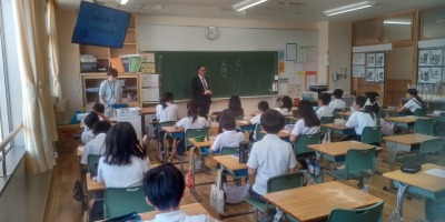 いじめ防止授業。教室で授業を受ける小学生たちと黒板の前に立つ講師の写真。