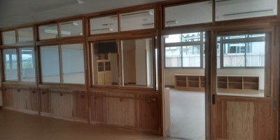 新校舎。がらんとした教室を廊下から撮影した写真。木製の仕切りと大きなガラス窓が特徴的。