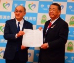 スーツを着用した男性2人が書類のようなものを両手で持ち前を向いている写真