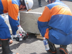 2人の消防団員がブロックの下を電動コンビツールを使って持ち上げようとしている写真