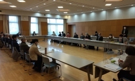 広いホールのような場所に長机が四角く配置され、沢山の職員が座り、会議をしている様子の写真