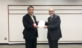 黒いスーツ姿の2名の男性が答申書を両手で前に見えるようにして2人で持っている様子の写真