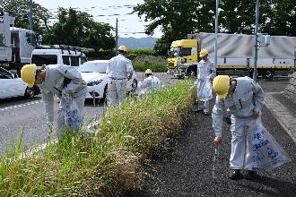 歩道にいるごみ袋とごみばさみを手にした人たちが側溝やガードレール裏のごみを拾い集めている様子の写真