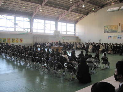 体育館内で児童たちと保護者たちがそれぞれ対面になり椅子に座っている写真