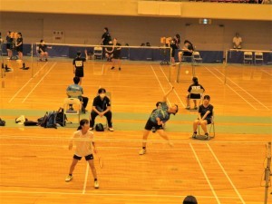 ジャンプしながらスマッシュを打っている選手とその前にラケットを持って待っている選手の写真