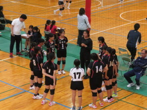 バレーボールのコートの隅で、ユニフォーム姿の複数の選手が輪になって話をしている写真